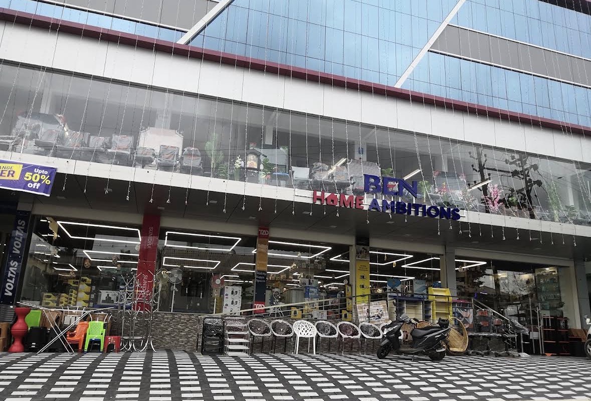 Corner BEN Home Ambitions showroom at blue hour with appliances visible through glass windows in Karimugal, Ernakulam